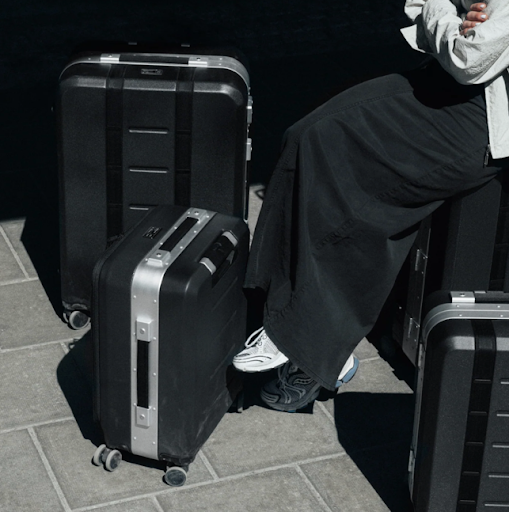 Person sitting on stacked black travel suitcases with hard shell luggage outdoors