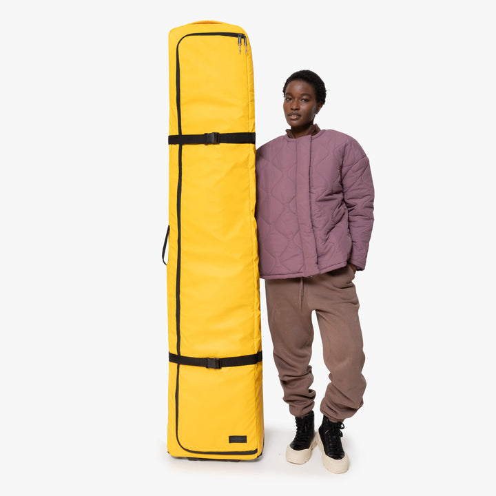 Person standing next to a yellow ski travel bag for size reference